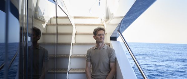 Arrival Yachts founder Nigel Wales sites on teak covered steps aboard a super yacht while looking seaward.